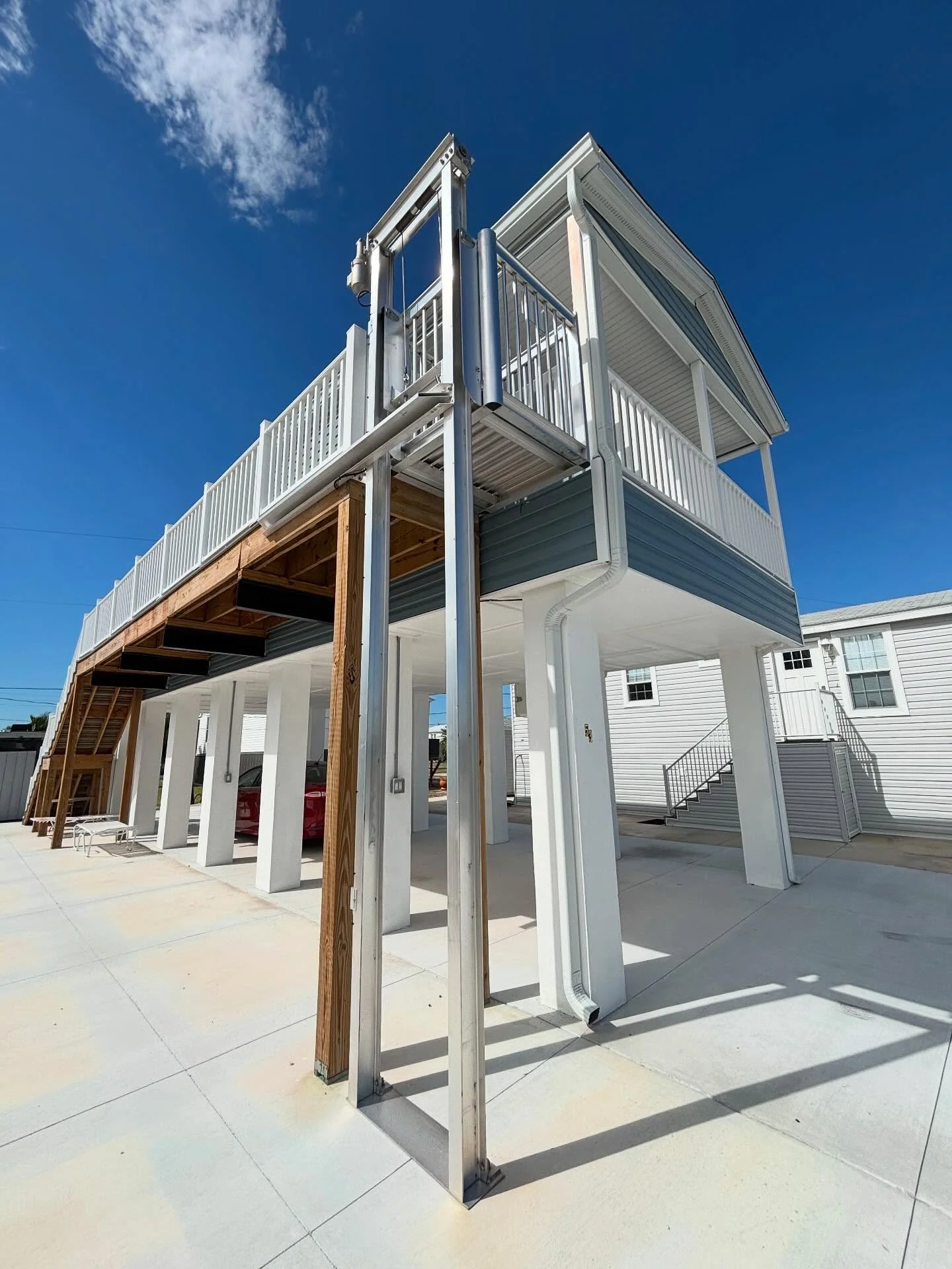Steel frame cargo lift with white columns, aluminum railings, and wooden staircase on concrete pad